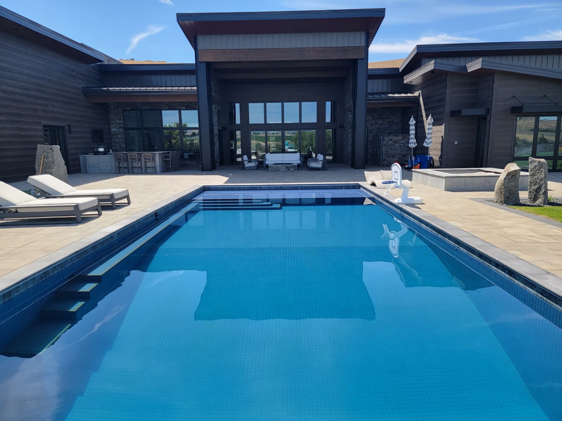 Dark navy all-tile lap pool with tanning ledge steps beside a modern black timber home in Washington
