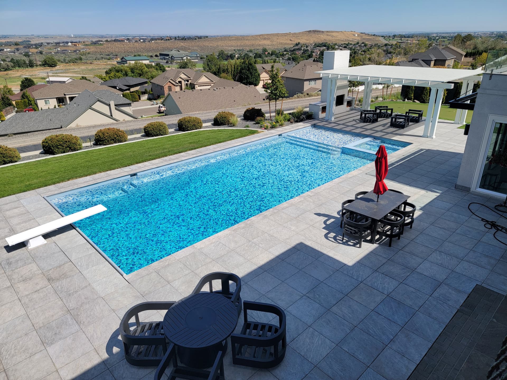 Aerial view of a mosaic all-tile pool with diving board, spa spillway, and valley views in Eastern Washington